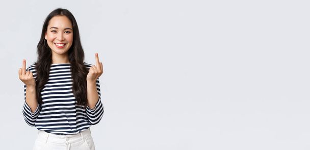 Lifestyle, beauty and fashion, people emotions concept. Unbothered and careless young happy smiling woman dont give a damn, showing middle fingers and feeling good, white background - Photo, Image