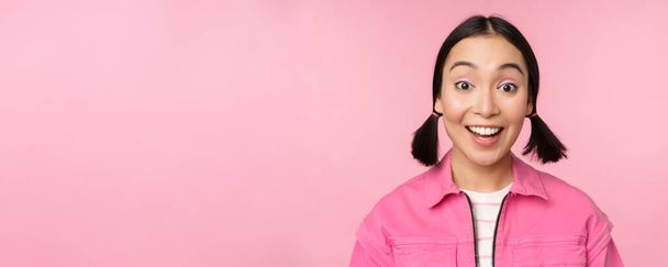 Közelkép portré gyönyörű ázsiai lány néz lelkes és mosolygós, nevető és mosolygós, álló boldog ellen rózsaszín háttér - Fotó, kép