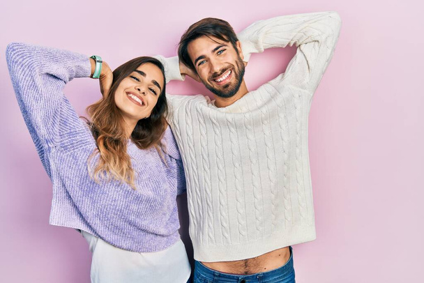 Junges hispanisches Paar in lässiger Kleidung entspannt sich und dehnt sich, Arme und Hände hinter Kopf und Hals lächeln glücklich  - Foto, Bild
