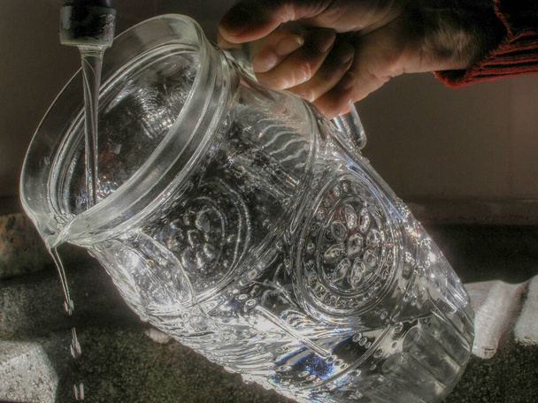 vízsugár, amely gyengéden beleesik egy üvegkancsóba egy csapból. - Fotó, kép
