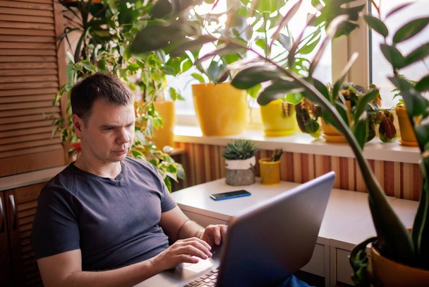 Ο άνθρωπος δουλεύει με φορητό υπολογιστή από το σπίτι. Μακρινός χώρος εργασίας με γραφείο εμπνευσμένο από την πράσινη φύση - Φωτογραφία, εικόνα