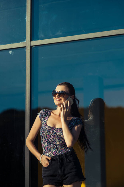 Cool girl speaks on tel. Beautiful girl in short shorts near the shop window. - Fotoğraf, Görsel
