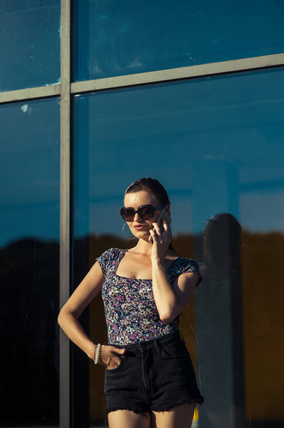 Cool girl speaks on tel. Beautiful girl in short shorts near the shop window. - Foto, Imagem