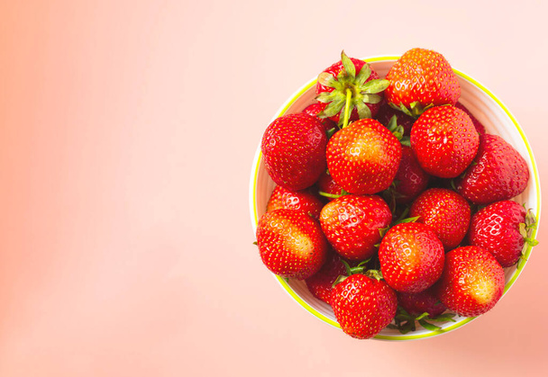 Vista desde arriba del plato con fresas rojas frescas rasgadas sobre fondo rosa. - Foto, Imagen