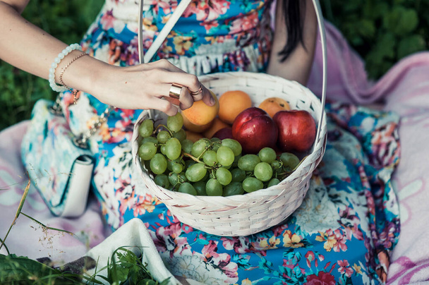 庭にリンゴを持つ女性。熟れた赤と緑のリンゴの完全なバスケットを持つ若い魅力的な女性は、リンゴの庭の芝生の上に横たわって笑顔です。収穫期だ。田舎暮らし. - 写真・画像