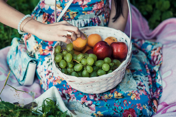 Woman with apples in the garden. Young attractive woman with a full basket of ripe red and green apples is lying on the grass in the apple garden and smiling. Harvest season. Country lifestyle. - 写真・画像