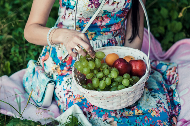 Woman with apples in the garden. Young attractive woman with a full basket of ripe red and green apples is lying on the grass in the apple garden and smiling. Harvest season. Country lifestyle. - Foto, Bild