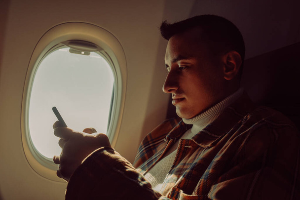 Ένας άντρας σε ένα μισοάδειο αεροπλάνο με τηλέφωνο. Guy ταξιδιώτη κοιτάζοντας smartphone. - Φωτογραφία, εικόνα