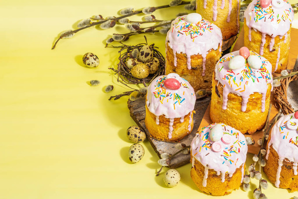 伝統的なイースターケーキ。アイシングと装飾が施されたお祭りの甘い食べ物。卵、巣、柳、流行のハードライト、暗い影。明るい黄色の背景に伝統的なベーキング、コピースペース - 写真・画像