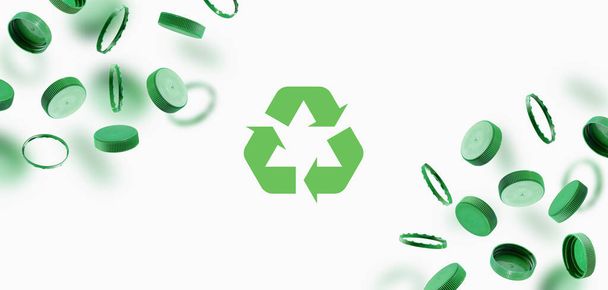 Zöld palack kupakok, újrahasznosítás szimbólum fehér alapon. Műanyag sapkák lebegnek a levegőben. A környezeti károktól való biztonság fogalma. A környezeti fenntarthatóság és a Föld Napja. - Fotó, kép