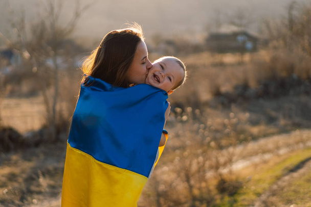 Donna abbraccia il suo piccolo figlio avvolto nella bandiera gialla e blu dell'Ucraina all'aperto. - Foto, immagini