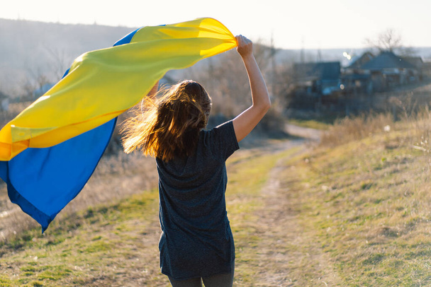 Woman holding a yellow and blue flag of Ukraine in outdoors - Фото, зображення