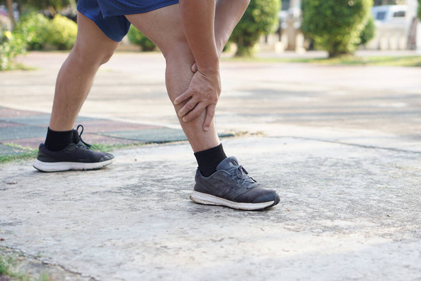 Runner uses hands to massage his sprain leg during exercise at the park. Concept : injury, sprain, painful from workout , exercise or sport.                 - Foto, Imagem