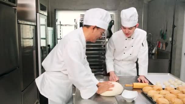 Два профессиональных азиатских повара-мужчины в белой униформе и фартуках смешивают тесто и яйца, готовят хлеб и свежую выпечку, пекут в духовке на кухне ресторана из нержавеющей стали. - Кадры, видео
