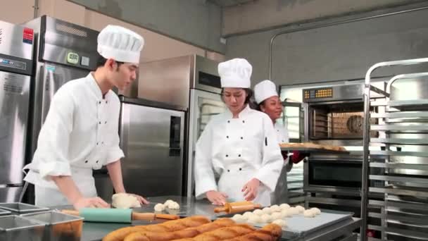 Professionelles Gourmet-Team, drei junge Köche in weißen Kochuniformen und Schürzen kneten Teig und Eier, bereiten Brot und frische Backwaren zu, backen im Ofen in der Edelstahl-Restaurantküche. - Filmmaterial, Video