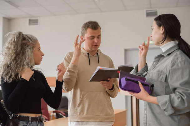 Two girls and a guy are talking in sign language. Three deaf students chatting in a university classroom. - Photo, Image