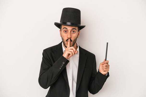 Young magician man holding wand isolated on white background keeping a secret or asking for silence. - Foto, Imagem