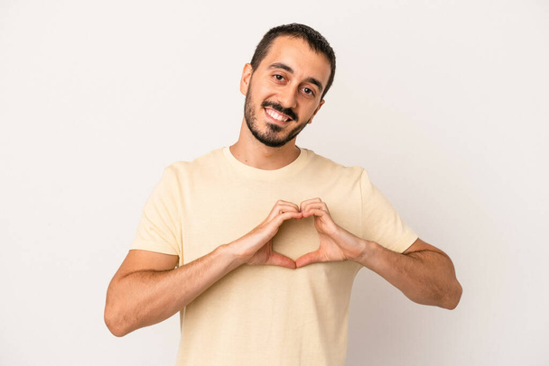 Giovane uomo caucasico isolato su sfondo bianco sorridente e mostrando una forma di cuore con le mani. - Foto, immagini