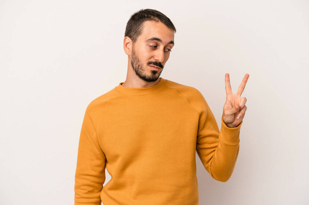 Young caucasian man isolated on white background joyful and carefree showing a peace symbol with fingers. - Foto, Imagen