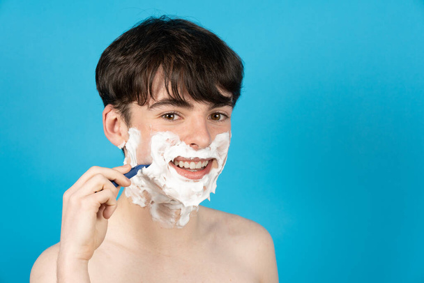 Happy teenager boy shaving face with foam and razor. - Φωτογραφία, εικόνα