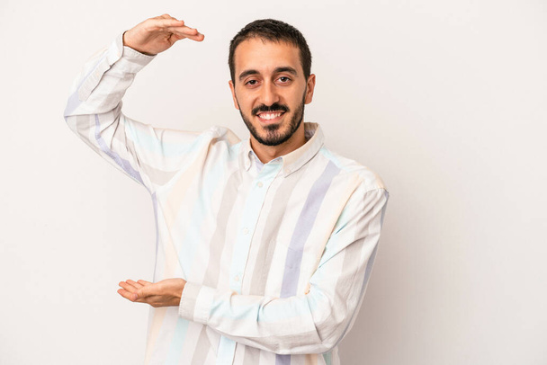 Young caucasian man isolated on white background holding something little with forefingers, smiling and confident. - Foto, Imagen