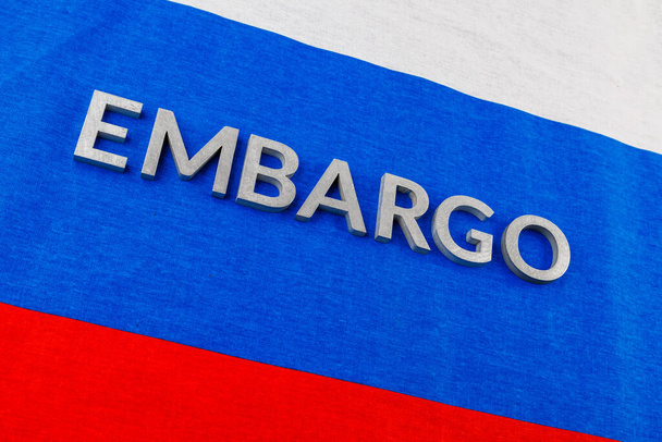 the word embargo laid with silver metal letters on russian tricolor flag in diagonal view - 写真・画像