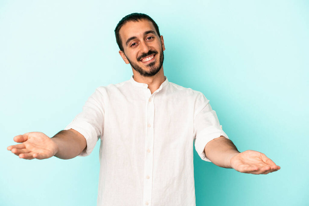 Young caucasian man isolated on blue background showing a welcome expression. - Photo, Image