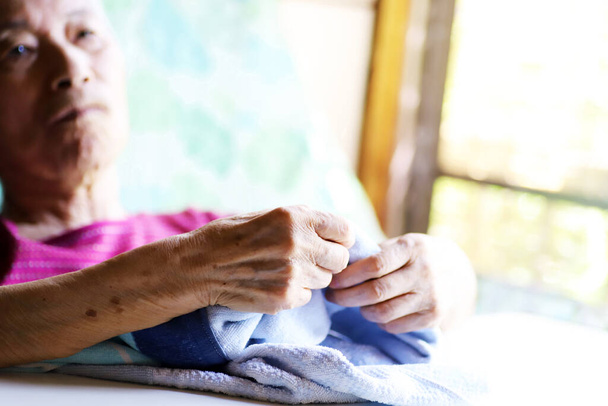 Літня жінка з деменцією сидить на ліжку для престарілих і грає з ковдрою
 - Фото, зображення