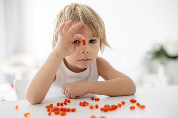 Cute little child, toddler boy, eating alfa omega 3 child suplement vitamin pills at home for better imunity - Foto, Bild
