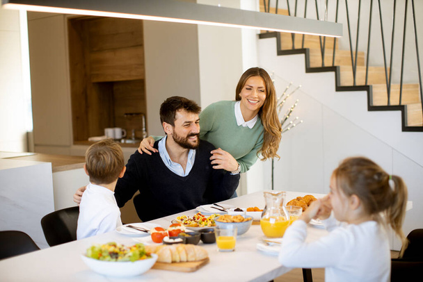Młoda szczęśliwa rodzina rozmawia podczas śniadania przy stole w mieszkaniu - Zdjęcie, obraz