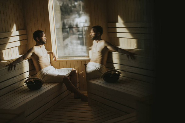 Handsome young man relaxing in the sauna and watching winter forest through the window - Photo, Image