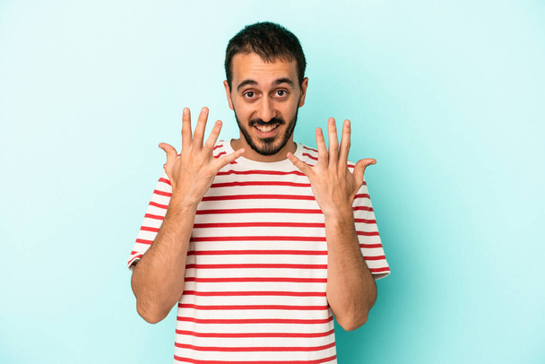 Νεαρός καυκάσιος άνδρας απομονωμένος σε μπλε φόντο, δείχνει το νούμερο δέκα με τα χέρια.. - Φωτογραφία, εικόνα
