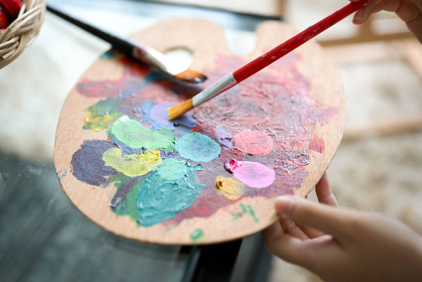 Close-up, Uma jovem segurando uma paleta de cores acrílicas, misturando a cor com seu pincel. - Foto, Imagem