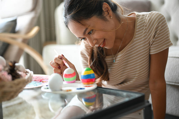 Attractive Asian woman admiring and painting her Easter egg with watercolour. Happy Easter holiday. - Photo, image