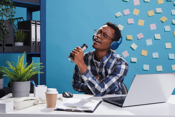 Cheerful smiling heartily young office worker wearing wireless headphones and listening to music - Photo, Image