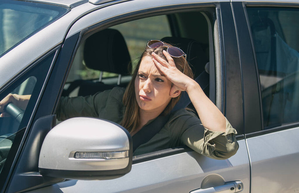 Νεαρή γυναίκα που κάθεται σε ένα αυτοκίνητο κολλημένη σε ένα μποτιλιάρισμα αισθάνεται αγχωμένη επειδή βιάζεται να πάει στη δουλειά. - Φωτογραφία, εικόνα