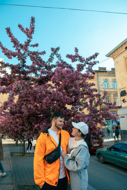 couple hugging posing taking photos outdoors in front of blooming tree copy space - Photo, Image