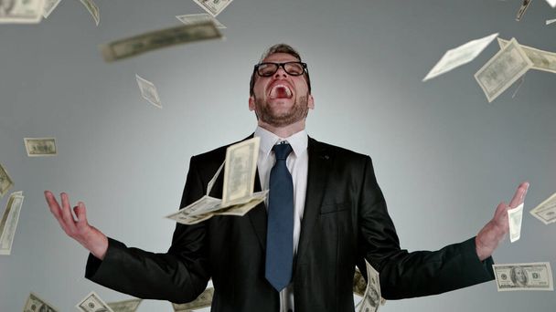 Close-up of screaming businessman with flying dollars banknotes isolated over gray background - Foto, Imagen