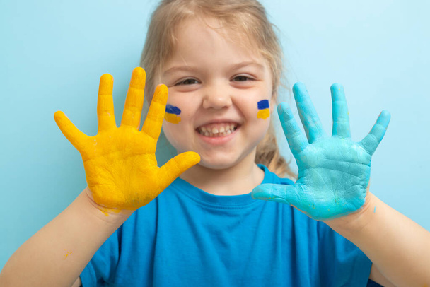 Sárga és kék festék a gyerektenyéren. Ukrán zászló szimbólum koncepció. Boldog ukrán lány. - Fotó, kép