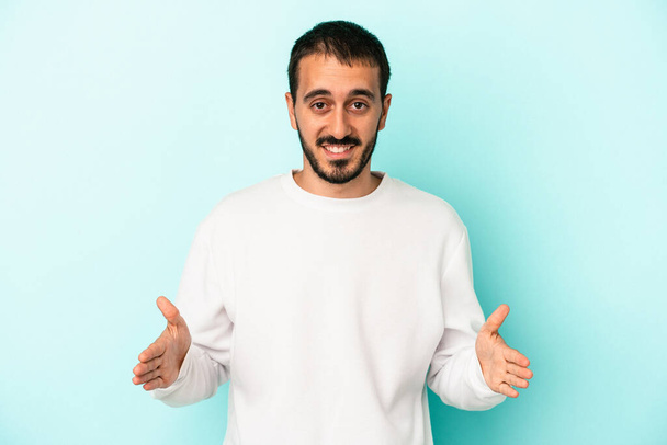 Νεαρός καυκάσιος άνδρας απομονωμένος σε μπλε φόντο κρατώντας κάτι και με τα δύο χέρια, παρουσίαση προϊόντος. - Φωτογραφία, εικόνα