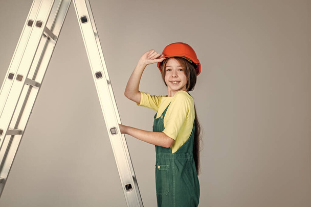 teen girl in uniform and helmet with ladder. female builder in hard hat. - Fotó, kép