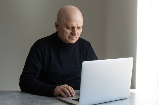 Idősebb férfi portréja otthon, aki laptopon dolgozik - Fotó, kép