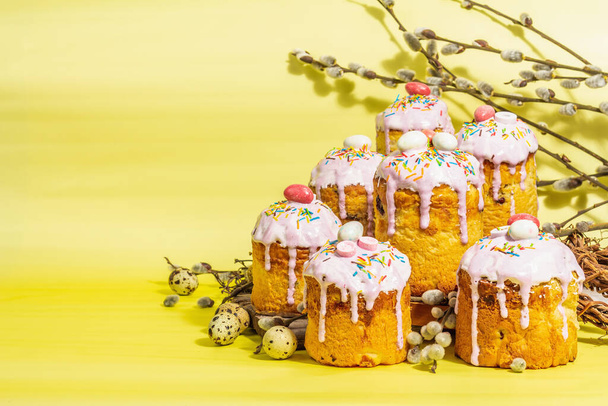 伝統的なイースターケーキ。アイシングと装飾が施されたお祭りの甘い食べ物。卵、巣、柳、流行のハードライト、暗い影。明るい黄色の背景に伝統的なベーキング、コピースペース - 写真・画像