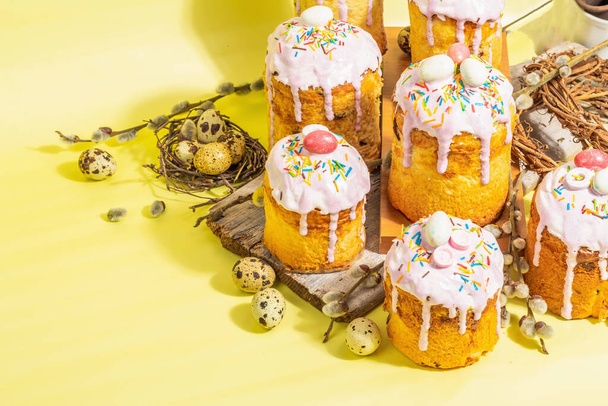 Traditional Easter cake. Festive sweet food with icing and decor. Eggs, nest, willow, trendy hard light, dark shadow. Traditional baking on bright yellow background, copy space - Фото, зображення