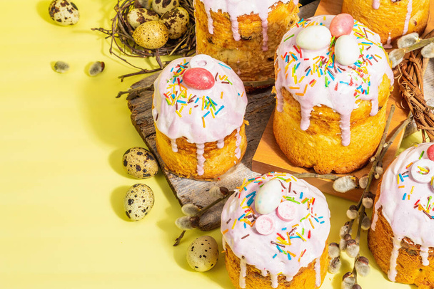 Traditional Easter cake. Festive sweet food with icing and decor. Eggs, nest, willow, trendy hard light, dark shadow. Traditional baking on bright yellow background, copy space - Foto, afbeelding