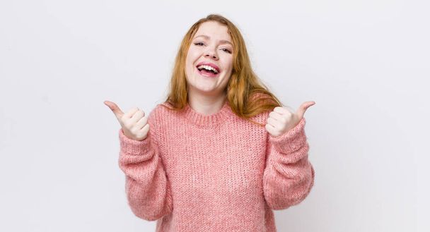 pretty red head woman smiling joyfully and looking happy, feeling carefree and positive with both thumbs up - Foto, imagen