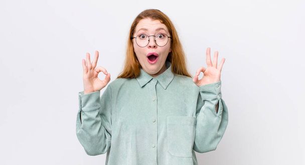 pretty red head woman feeling shocked, amazed and surprised, showing approval making okay sign with both hands - Photo, image