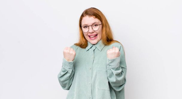 pretty red head woman shouting triumphantly, laughing and feeling happy and excited while celebrating success - Foto, afbeelding