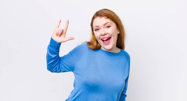 pretty red head woman feeling happy, fun, confident, positive and rebellious, making rock or heavy metal sign with hand - Photo, Image