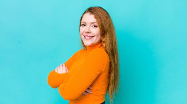 pretty red head woman smiling to camera with crossed arms and a happy, confident, satisfied expression, lateral view - Foto, afbeelding